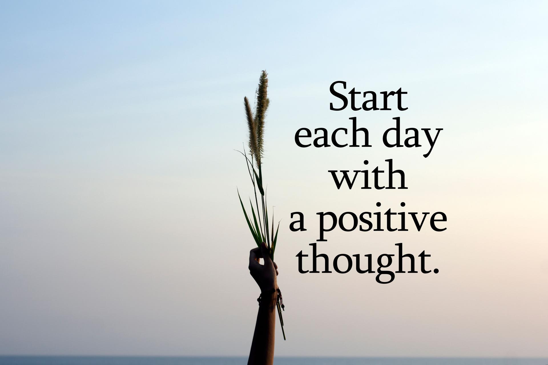 Start each day with a positie thought. With person holding flower plant in hand on blue sky background.